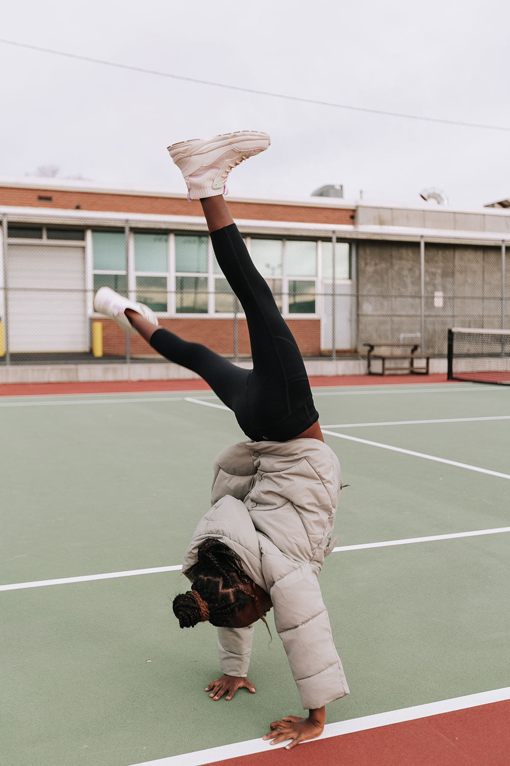 Young girl doing a handstand on a tennis court wearing Everyway kids activewear. Featuring black Longline Crop and All Day Leggings.