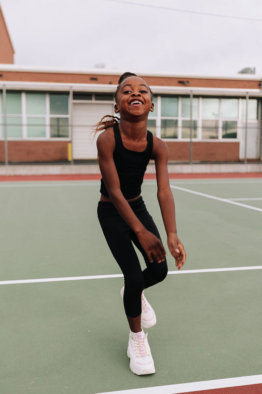 Young girl on a tennis court wearing Everyway kids activewear. Featuring black Longline Crop and All Day Leggings.