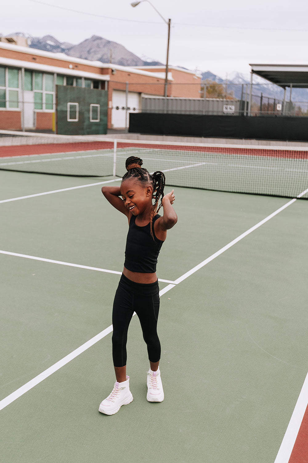 Young girl on a tennis court wearing Everyway kids activewear. Featuring black Longline Crop and All Day Leggings.
