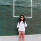 Young girl on a tennis court wearing Everyway kids activewear. Featuring a White Daily Tee and Dusty Rose All Day Leggings.
