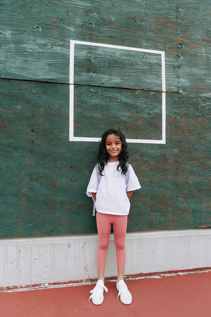 Young girl on a tennis court wearing Everyway kids activewear. Featuring a White Daily Tee and Dusty Rose All Day Leggings.