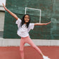 Young girl on a tennis court wearing Everyway kids activewear. Featuring a White Daily Tee and Dusty Rose All Day Leggings.